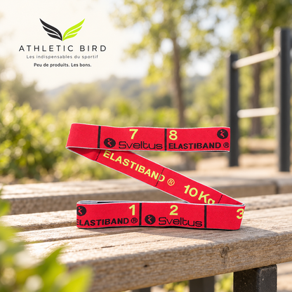 Elastiband Sveltus rouge 10 kg posé sur un banc en bois près d’un espace sportif extérieur, avec logo Athletic Bird