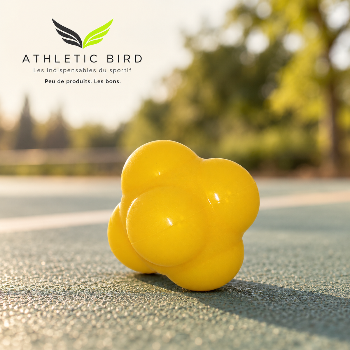 Balle de réactivité Sveltus jaune sur un sol sportif extérieur, avec des arbres en arrière-plan et le logo Athletic Bird