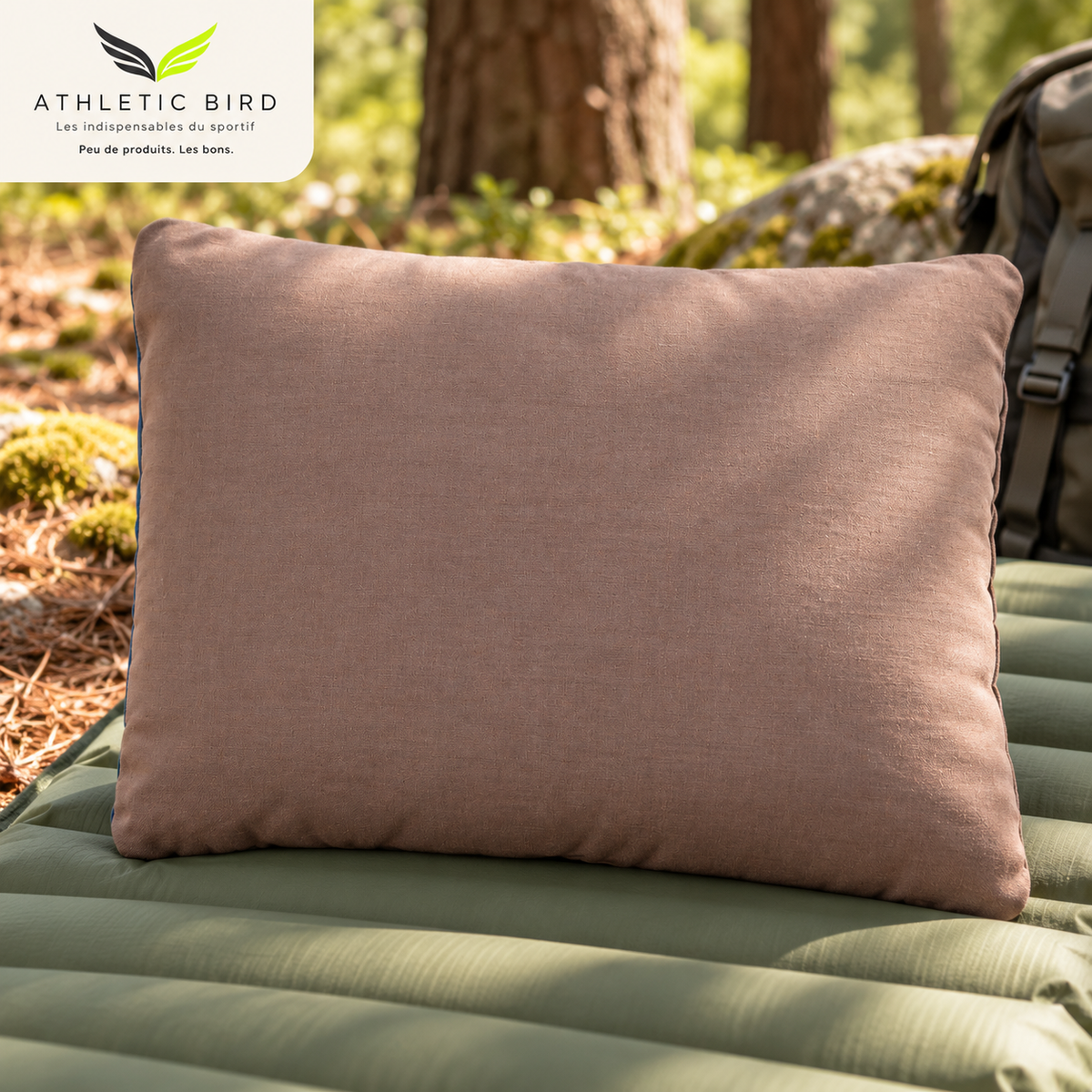 Coussin de randonnée Wilsa Outdoor taupe posé sur un matelas de camping en forêt, avec logo Athletic Bird en haut à gauche